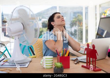 Weibliche Führungskraft genießt eine Brise vom Tischventilator Stockfoto