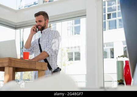Ein Geschäftsmann, der auf dem Mobiltelefon spricht, während er am Schreibtisch steht, aus der Perspektive des Blickwinkels Stockfoto