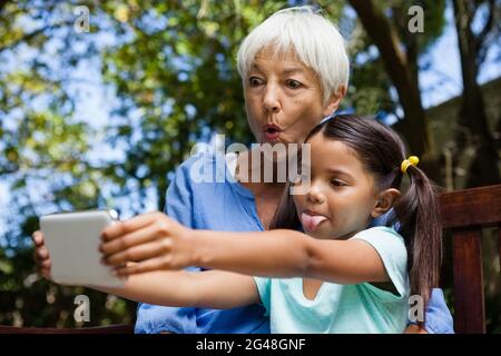 Großmutter und Enkelin machen sich beim Selfie auf der Bank ein Gesicht Stockfoto