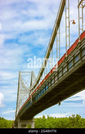 Eine moderne Fußgängerbrücke aus Eisen mit Kabelgefüge und einer Laterne vor einem blau bewölkten Himmel am Sommertag. Blick von unten auf einen Hig Stockfoto