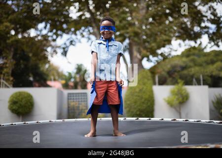 Junge im Superhelden-Kostüm auf Trampolin stehend Stockfoto