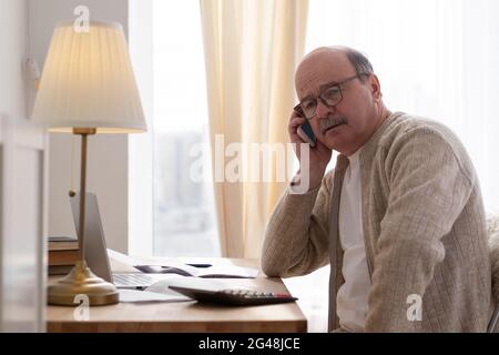 Älterer Mann, der am Telefon telefoniert und zu Hause am Tisch sitzt Stockfoto