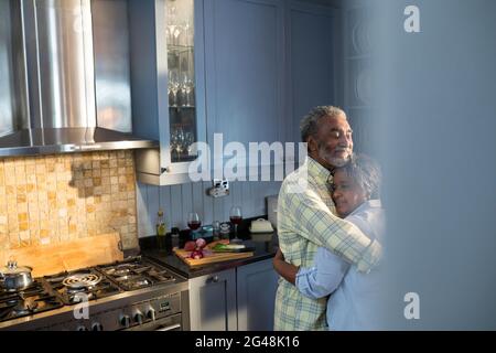 Liebevoll lächelndes Paar, das sich umarmt, während es in der Küche steht Stockfoto