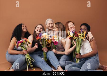 Gruppe von multiethnischen Frauen, die im Studio zusammen sitzen. Sechs lächelnde Weibchen mit Blumensträußen. Stockfoto