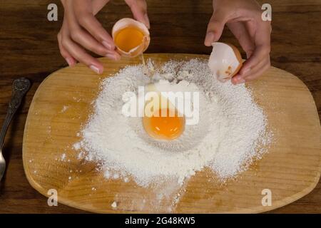 Mann bricht Eier im Mehl auf Holzbrett Stockfoto