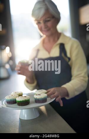 Ältere Frau holt den Cupcake vom Tablett Stockfoto