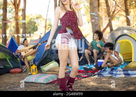 Junge Frau, die auf dem Feld steht, mit Freunden, die im Hintergrund an Zelten sitzen Stockfoto