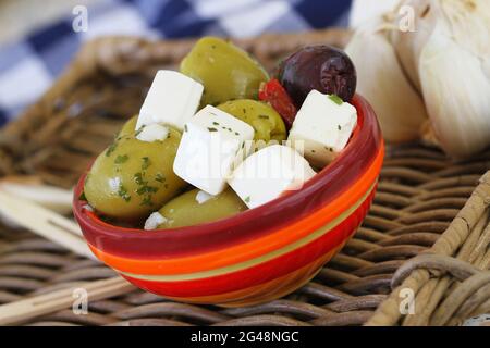 Leckere grüne und schwarze Oliven mit Feta-Käsestücken in einer bunten Tonschüssel, Nahaufnahme Stockfoto