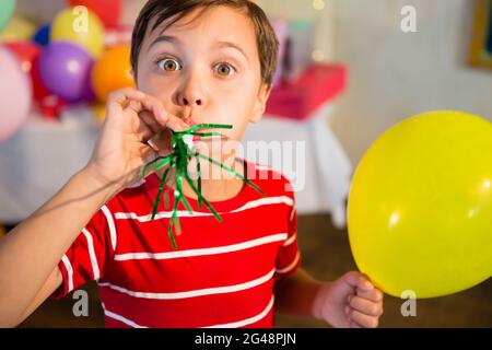 Niedlicher Junge weht Party Horn während der Geburtstagsfeier Stockfoto