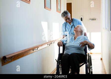 Krankenschwester spricht, während sie den Patienten im Rollstuhl sitzend schiebt Stockfoto