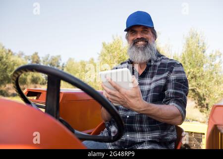 Porträt eines glücklichen Mannes mit digitalem Tablet im Traktor Stockfoto