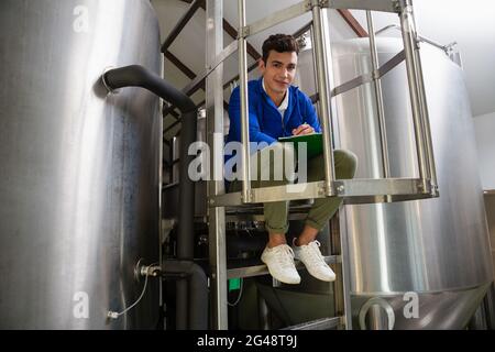 Porträt des Arbeiters in voller Länge inmitten von Lagertanks, die auf die Zwischenablage schreiben Stockfoto