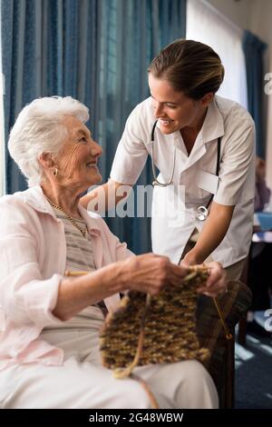 Lächelnde ältere Frau strickt, während sie eine Ärztin anschaut Stockfoto