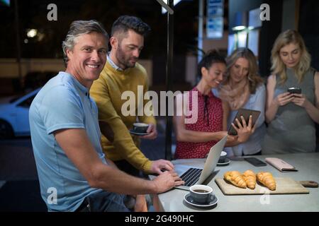 Freunde, die beim Kaffee elektronische Geräte benutzen Stockfoto
