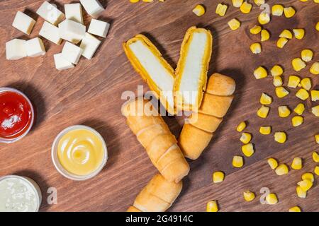 Venezolanischer Käse-Tequenos auf einem Holzboden mit Saucen und geschältem Mais halbiert. Stockfoto