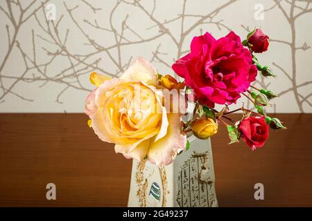 Foto eines Straußes natürlicher Blumen in einer Vase auf braunem Papierhintergrund und einem Holzsockel.das Foto wurde im horizontalen Format aufgenommen und ist inte Stockfoto