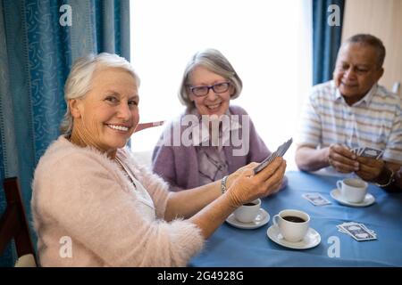 Lächelnde ältere Freunde spielen beim Kaffee Karten Stockfoto