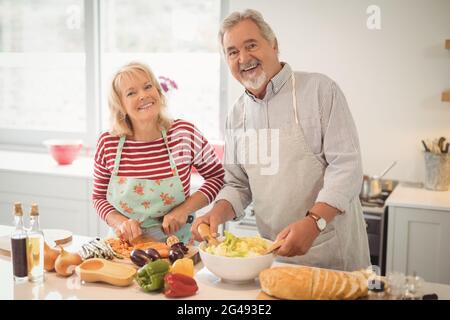 Lächelndes Seniorenpaar, das in der Küche Salat zubereitet Stockfoto