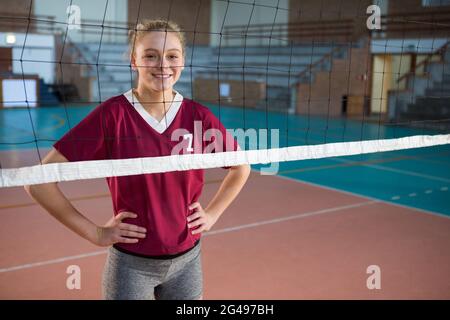 Lächelnde Volleyballspielerin, die auf dem Platz mit der Hand auf den Hüften steht Stockfoto