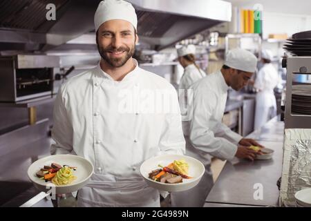 Der lächelnde Koch hält ein köstliches Gericht in der Küche Stockfoto