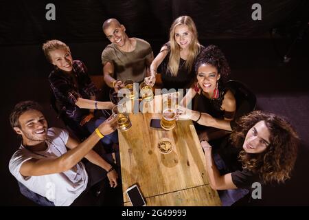 Hochwinkelportrait von glücklichen Freunden, die am Tisch toasten Stockfoto