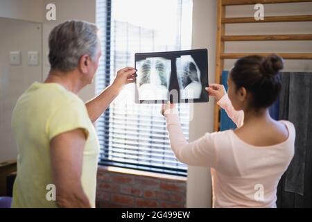 Rückansicht eines älteren männlichen Patienten und einer weiblichen Therapeutin beim Betrachen der Röntgenaufnahme Stockfoto