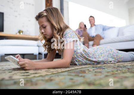 Tochter mit digitalem Tablet im Wohnzimmer, während die Eltern auf dem Sofa sitzen Stockfoto