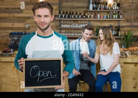 Kellner hält eine Tafel mit offenem Schild und der Kunde im Hintergrund Stockfoto