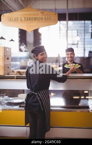 Porträt eines lächelnden jungen Kellners und einer Kellnerin, die Teller an der Theke hält Stockfoto