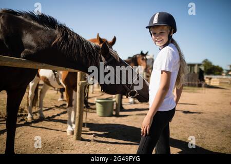 Lächelndes Mädchen, das in der Nähe des Pferdes auf der Ranch steht Stockfoto