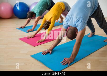 Instruktor, der die Schüler beim Üben der nach unten schauenden Hundehaltung im Yoga-Studio begleitet Stockfoto