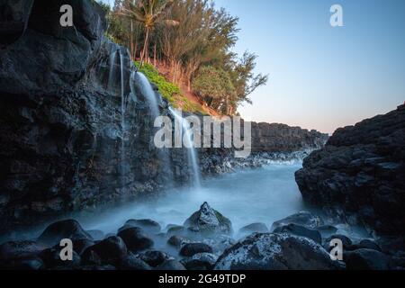 PRINCEVILLE, HAWAII, VEREINIGTE STAATEN - 01. Jun 2021: Queen's Bath Wasserfall stürzt von einem Bach in einen Stein, der in die Lavaküste auf Kauais n geschnitten ist Stockfoto