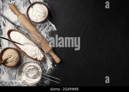 Verschiedene Arten von Mehl in Holzschalen auf schwarzem Tisch, Draufsicht Stockfoto