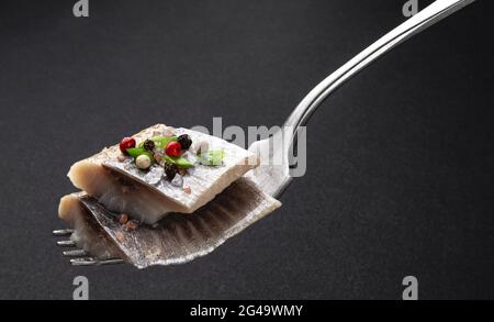 Stücke von gesalzenem Hering auf Gabel auf schwarzem Hintergrund Stockfoto