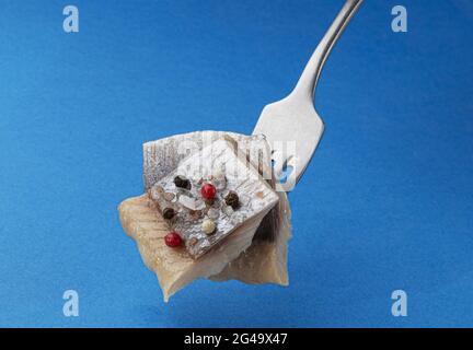 Stücke von gesalzenem Hering auf Gabel isoliert auf blauem Hintergrund Stockfoto