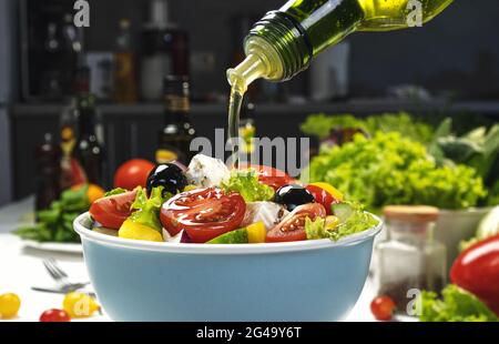 Gießen von Olivenöl auf frischem Gemüsesalat, griechischer Salat auf weißem Tisch Stockfoto