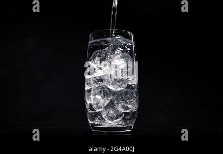 Wasser in Glas mit zerkleinertem Eis auf schwarzem Hintergrund gießen Stockfoto
