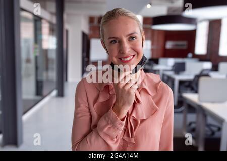 Porträt einer kaukasischen Geschäftsfrau mit gesenkter Gesichtsmaske, die im Büro steht und lächelt vor der Kamera Stockfoto
