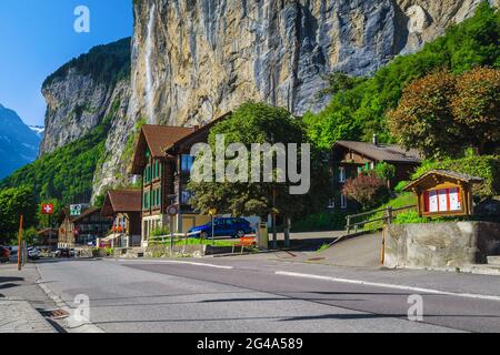 Malerische Straße mit Chalets und hohem Staubbach-Wasserfall im Hintergrund. Alpine Holzhäuser und atemberaubender Blick auf die Straße in Lauterbrunnen, Berner ob Stockfoto