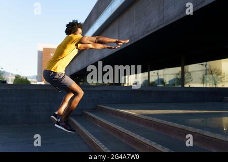 Schwarzer Mann tut Kniebeugen mit Springen auf einem Schritt. Stockfoto