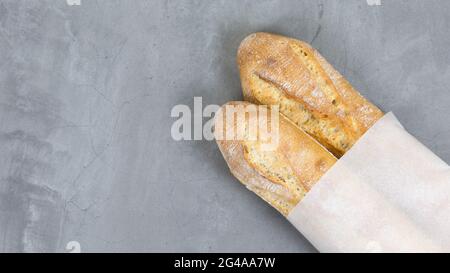 Nahaufnahme testy französisch Baguettes, gebackenes Brot auf grauen Stein Tisch Hintergrund. Umweltfreundliche Papierverpackung. Copy space Stockfoto