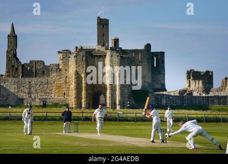 Am Samstagabend wird im Warkworth Cricket Club ein Cricket-Spiel gespielt, wobei die Ruinen des mittelalterlichen Warkworth Castle als Rückfall in Warkworth, Morpeth, Northumberland, zu sehen sind. Bilddatum: Samstag, 19. Juni 2021. Stockfoto