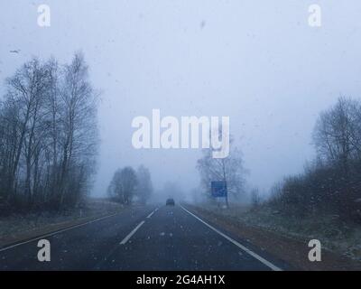 Asphaltstraße und Wolken am Himmel. Schneefall im Winter. Stockfoto