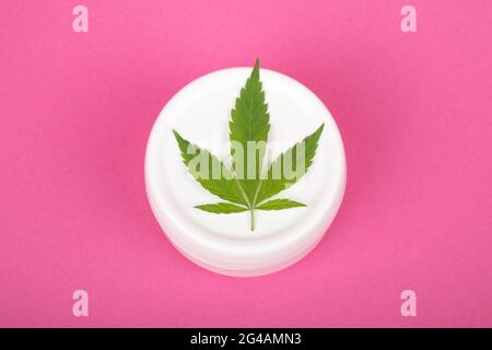 Kosmetik mit Marihuanaextrakt, Feuchtigkeitscreme mit Cannabisblatt auf rosa Hintergrund Nahaufnahme. Stockfoto