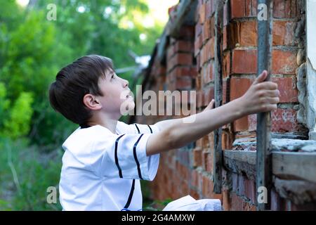 Ein Teenager in einem weißen T-Shirt steht gegen eine alte Backsteinmauer und schaut nach oben. Selektiver Fokus. Hochformat Stockfoto