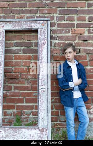 Ein modisch gekleideter Kerl in einem blauen Hemd steht an einer alten verwitterten Tür gegen eine Ziegelwand. Nahaufnahme. Selektiver Fokus. Hochformat Stockfoto
