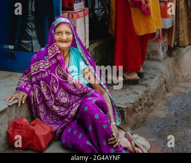 Ältere Frau in farbenfrohen traditionellen indischen Kleidern, die sich vom Spaziergang entlang der Straße in Delhi, Indien, ausruhen. Stockfoto