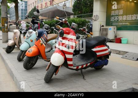 Vier bunte Motorroller parkten in einer Linie auf einem Bürgersteig im Bezirk Dongcheng, Peking, China Stockfoto