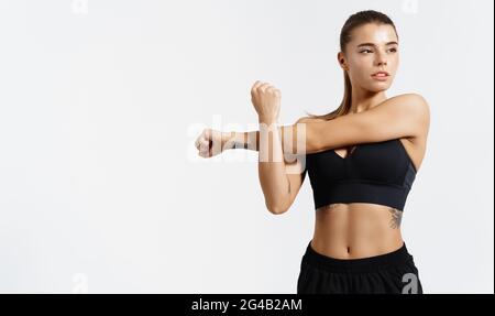 Entschlossene, starke und gesunde Sportlerin, dehnt, streckt ihre Arme, wärmt sich für das Training im Fitnessstudio auf, schaut weg. Silhouette eines jungen Athleten Stockfoto