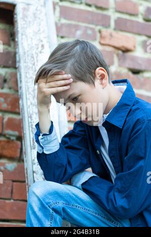 Ein modisch gekleideter Kerl in einem blauen Hemd steht an einer alten verwitterten Tür gegen eine Ziegelwand. Nahaufnahme. Selektiver Fokus. Hochformat Stockfoto